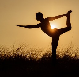 Woman does yoga pose in front of setting sun