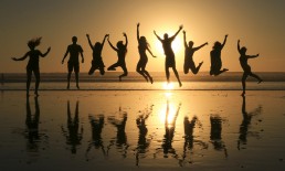 Silhouettes of a joyful team leaping on tropical beach with setting sun behind them