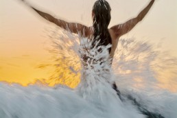 Woman at play jumps into wave at sunset.