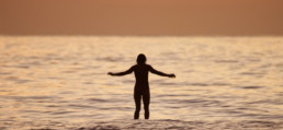 Woman stands on a surfboard at sunset.