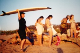 A man holds a surf board with his family on a beach