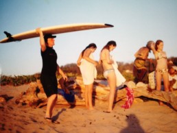 A man holds a surf board with his family on a beach