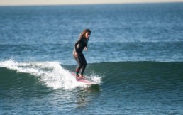 African American woman surfs a blue wave on a longboard.