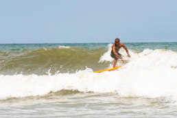 African American man surfs a waist high wave on a yellow single fin longboard